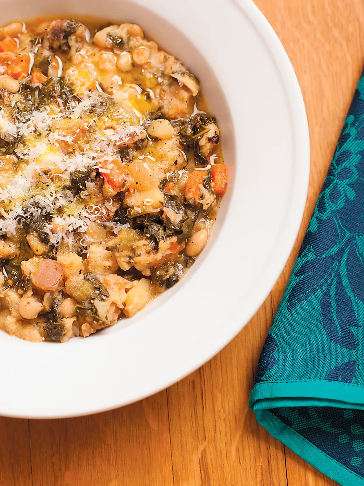 White bowl off Ribollita on wooden table with green napkin.