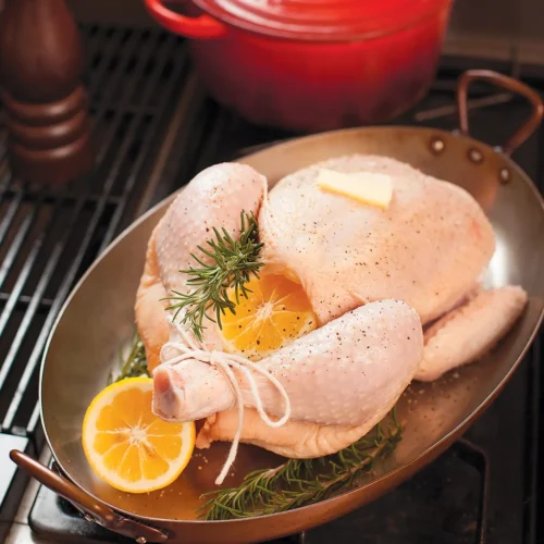 Uncooked trussed chicken in oval roasting pan getting ready to go into the oven to roast.