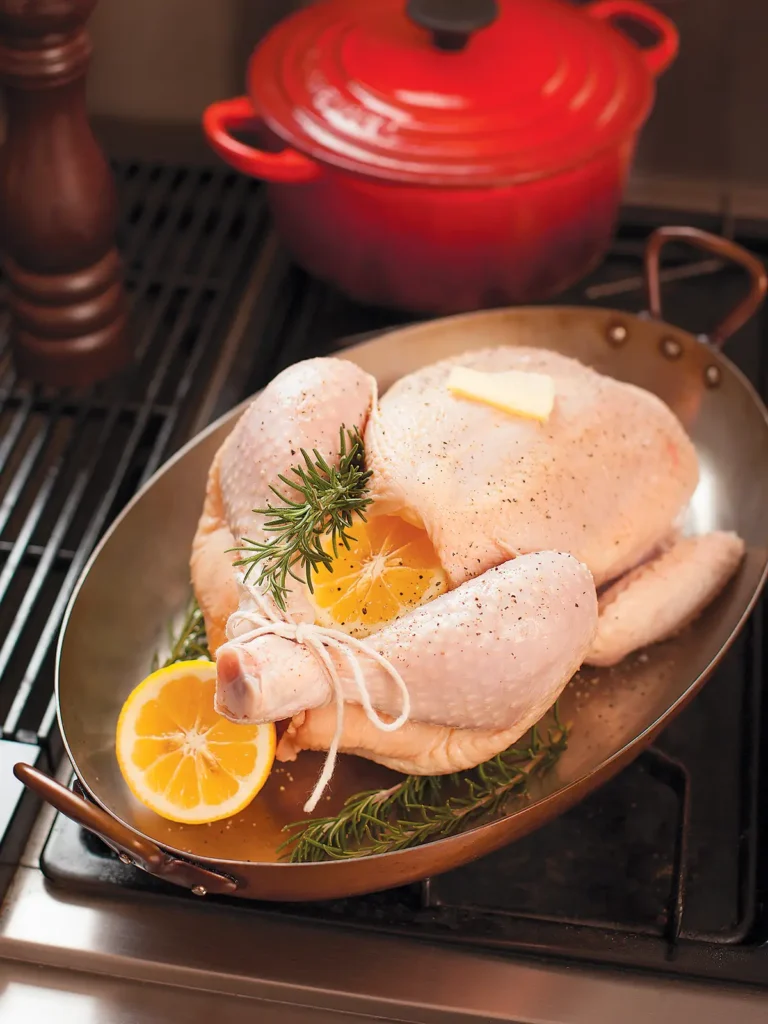 Uncooked trussed chicken in oval roasting pan getting ready to go into the oven to roast.