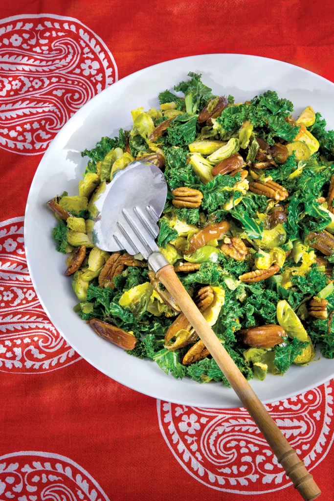 Roasted Kale, Brussels Sprouts, Date and Pecan Salad in a white bowl on a red patterned tablecloth.