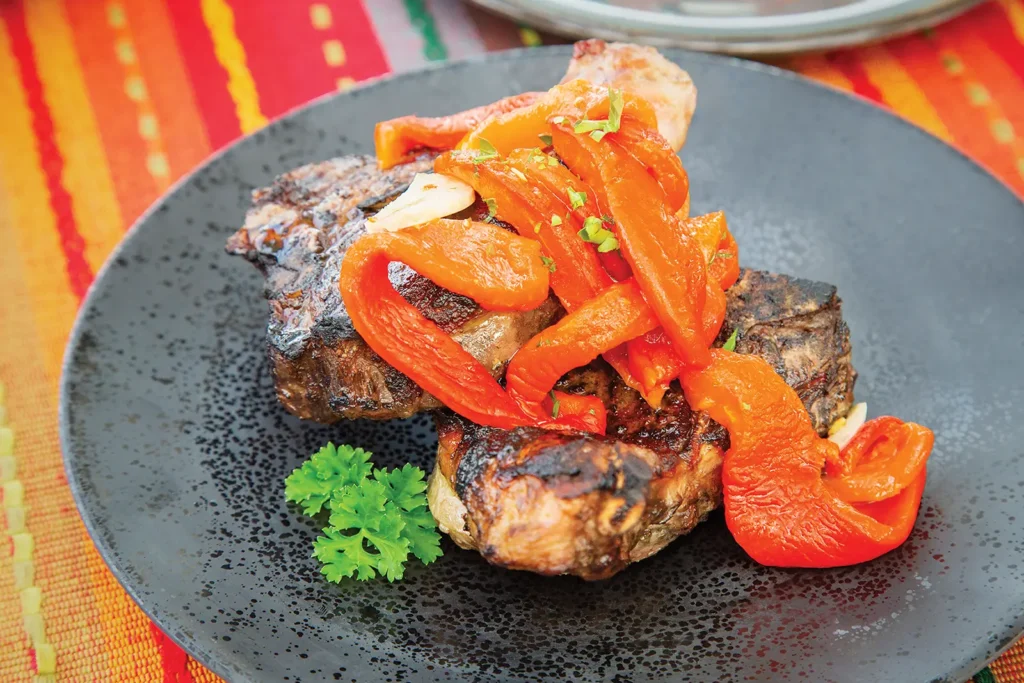 Roasted red peppers on top of grilled lamb chops on a round plate.