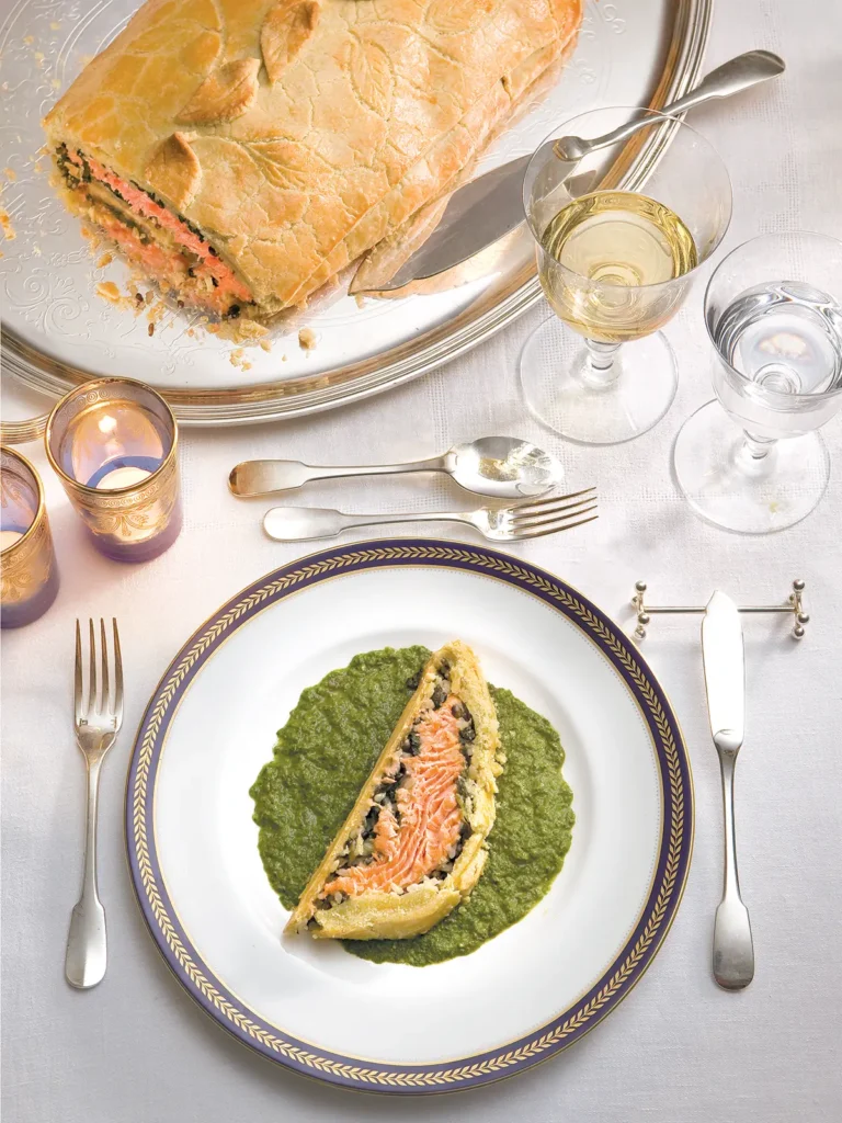 Salmon Coulibiac on a platter with a slice placed on a bed of herb and chive coulis.