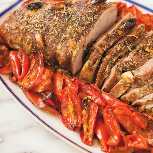 Stufffed Provençal Leg of Lamb sliced and arranged on an oval serving platter with roasted Roma tomatoes.