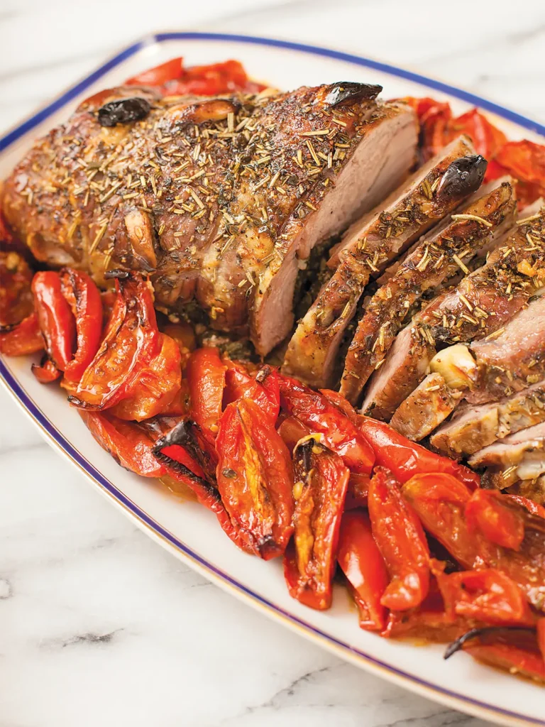 Stufffed Provençal Leg of Lamb sliced and arranged on an oval serving platter with roasted Roma tomatoes.