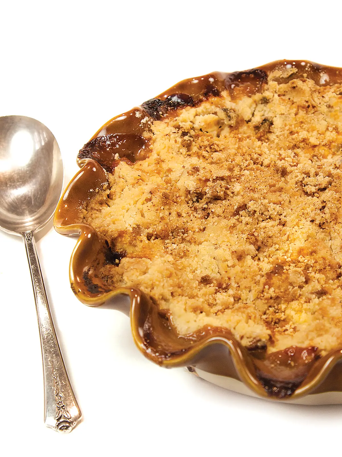 Apple crumble in a baking dish next to a silver spoon.