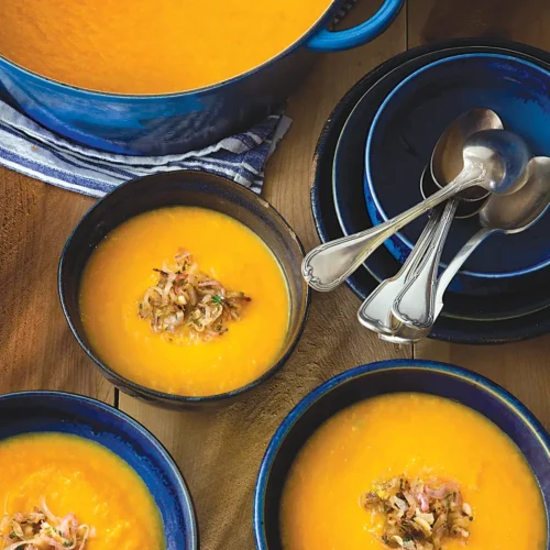 Tablescape with bowls of carrot and leek soup with zesty shallots.