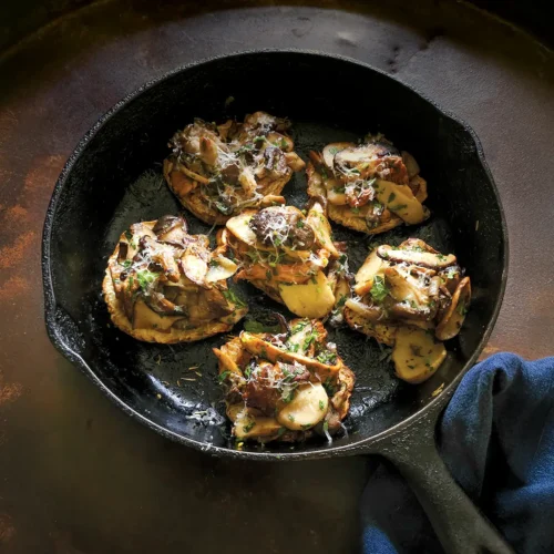 Cast iron skillet with 6 celeriac steaks topped with sautéed wild mushrooms.