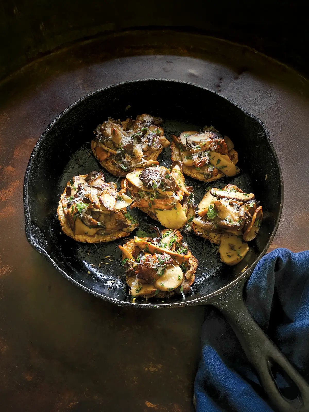 Cast iron skillet with 6 celeriac steaks topped with sautéed wild mushrooms.