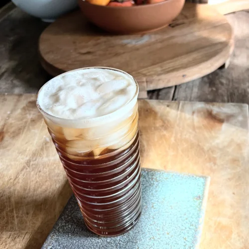 A glass of espresso ginger soda on a wooden cutting board.