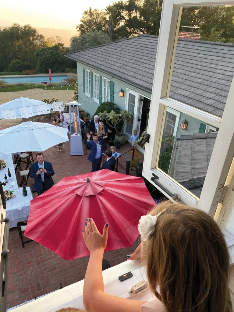 Little girl looking out over a family wedding and waving from a second floor window.