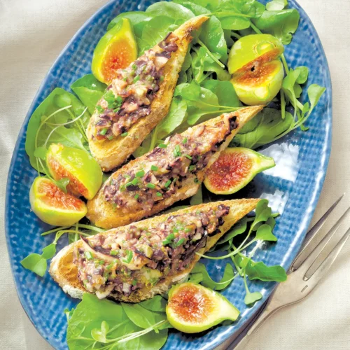 Oval platter with fig and tapenade crostini atop watercress salad.