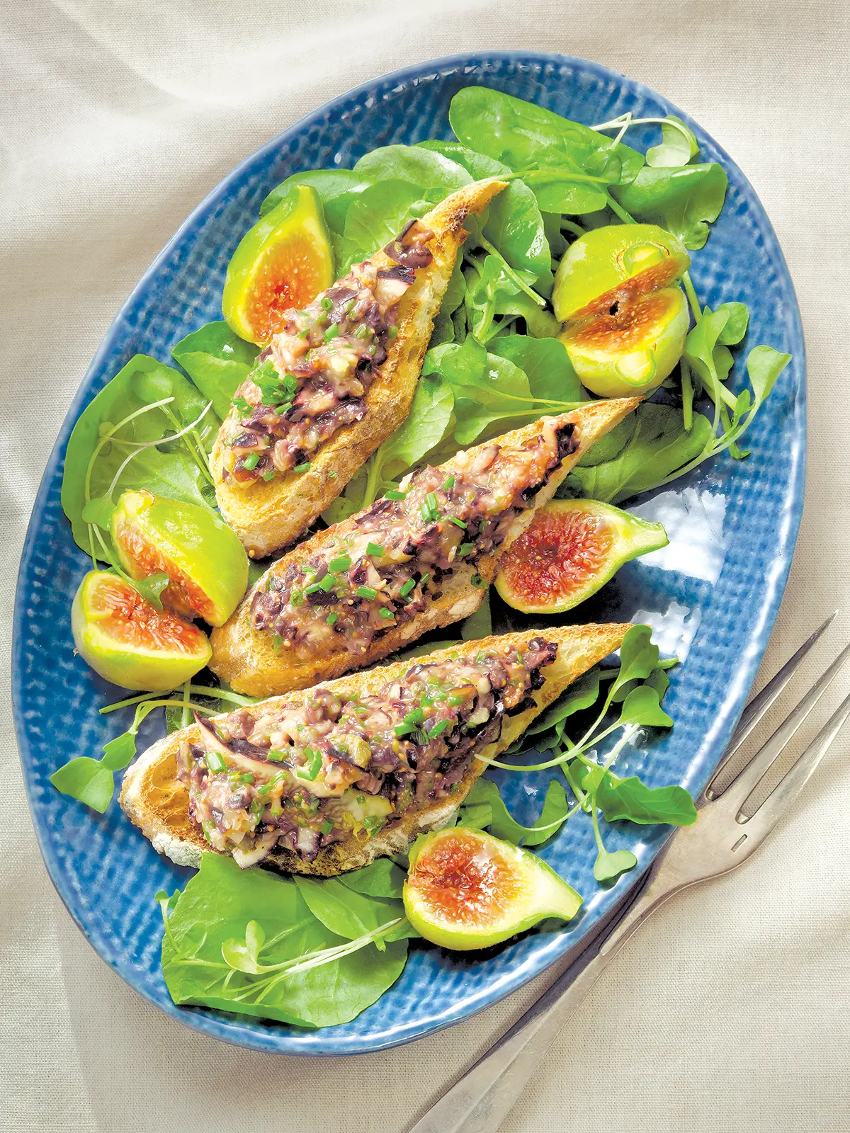 Oval platter with fig and tapenade crostini atop watercress salad.