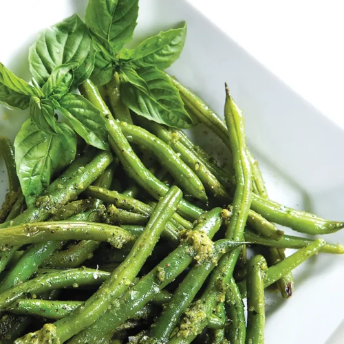 Rectangular plate with green beans topped with pesto.