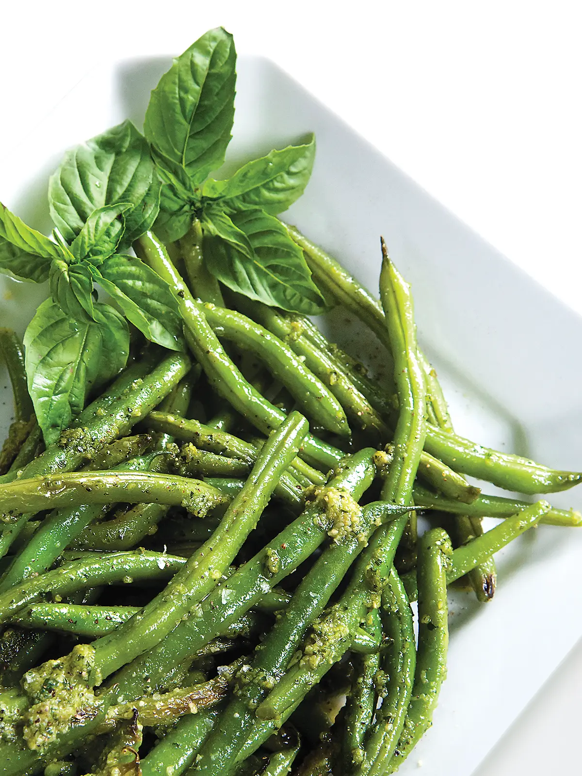 Rectangular plate with green beans topped with pesto.