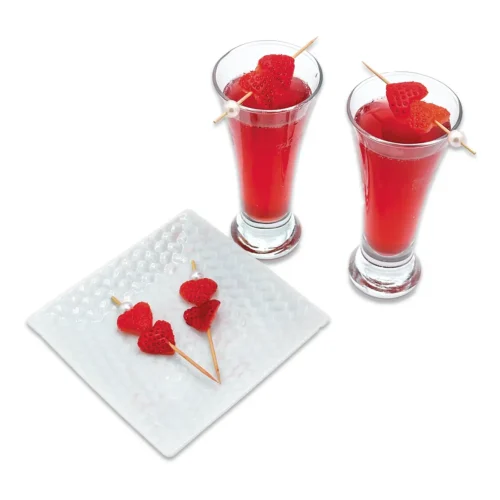 Two hibiscus tonic concoction cocktails next to a plate with heart shaped strawberries on toothpicks.