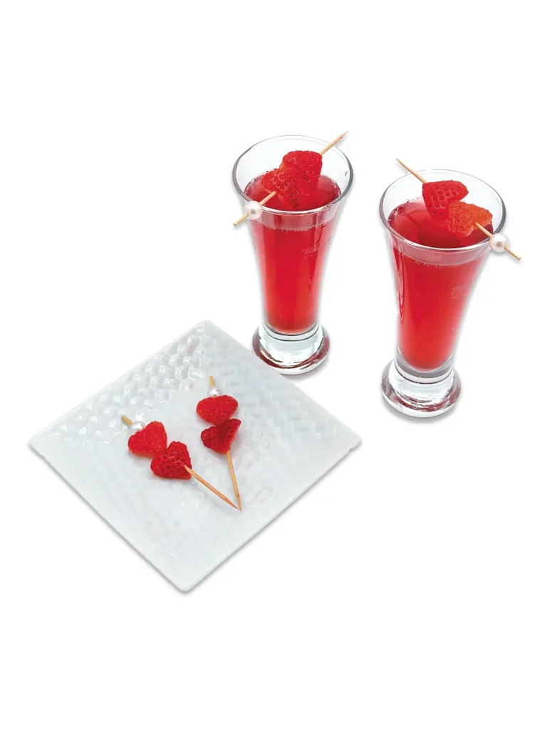 Two hibiscus tonic concoction cocktails next to a plate with heart shaped strawberries on toothpicks.