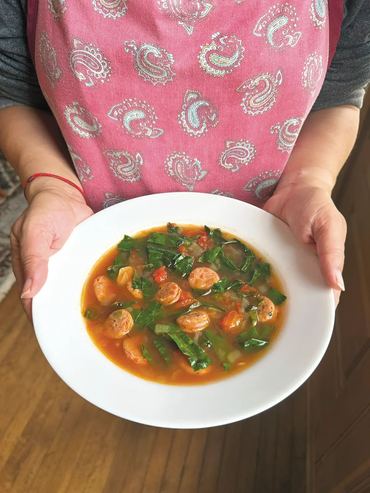 Woman holding a bowl of kale and sausage soup in front of her.