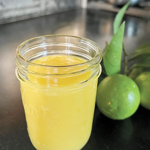 A half pint mason jar of lemon lime curd with a whole lime next to it.
