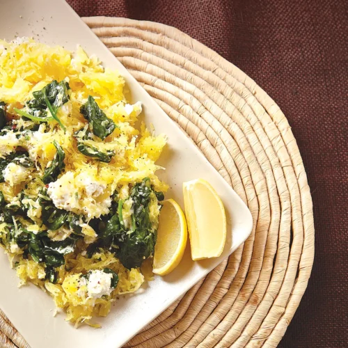 Rectangular dish containing Lemony Spaghetti Squash with Goat Cheese and Spinach on a round ratan placement.