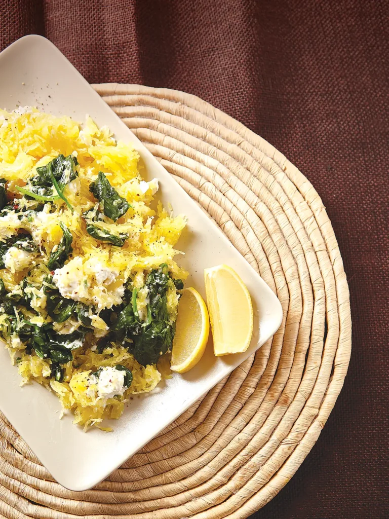 Rectangular dish containing Lemony Spaghetti Squash with Goat Cheese and Spinach on a round ratan placement.