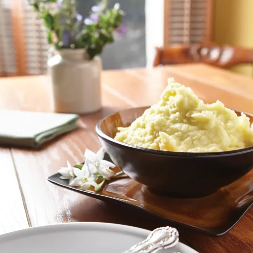 Tablescape with a round bowl of mashed potatoes on a square plate.