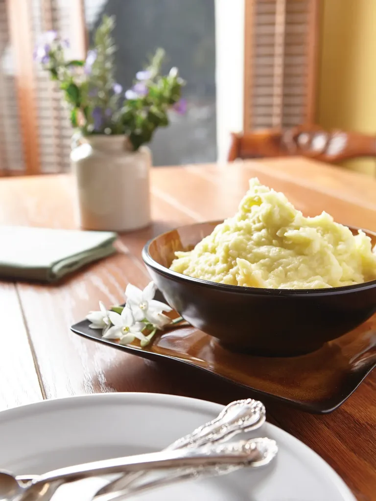 Tablescape with a round bowl of mashed potatoes on a square plate.