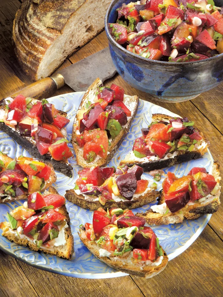 Tablescape with 8 pieces of pluot bruschetta arranged on a round plate.