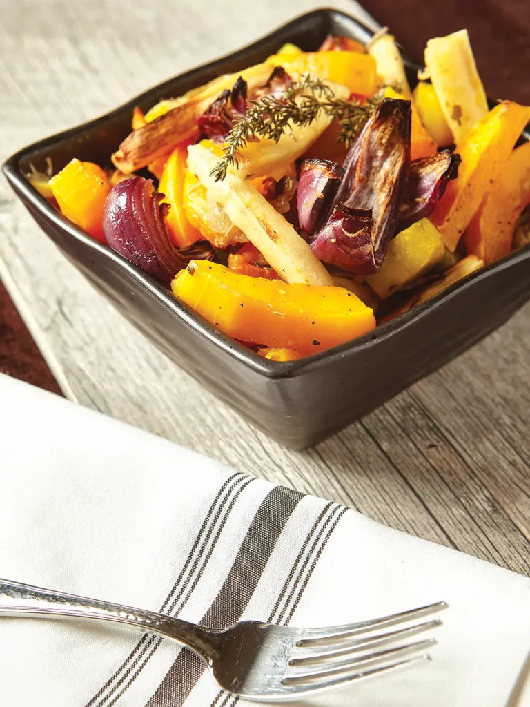 Square bowl with roasted root vegetables next to a fork on a linen napkin.