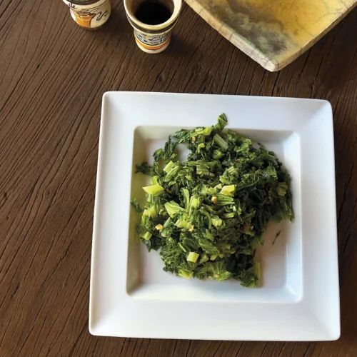 A square white plate piled with sauteed curly mustard greens.