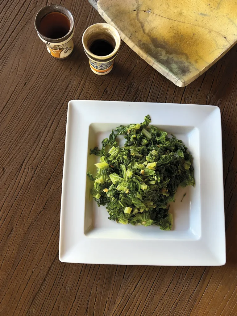 A square white plate piled with sauteed curly mustard greens.