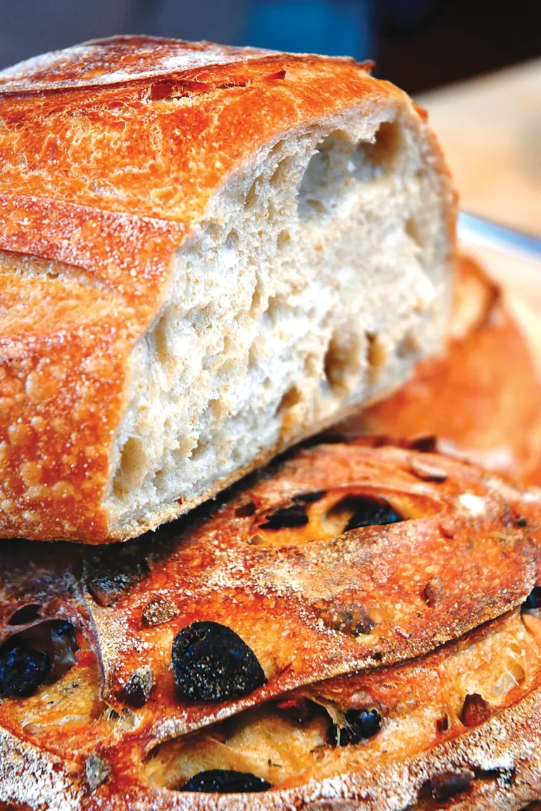 A cut loaf of olive bread with a slice laying by its side.