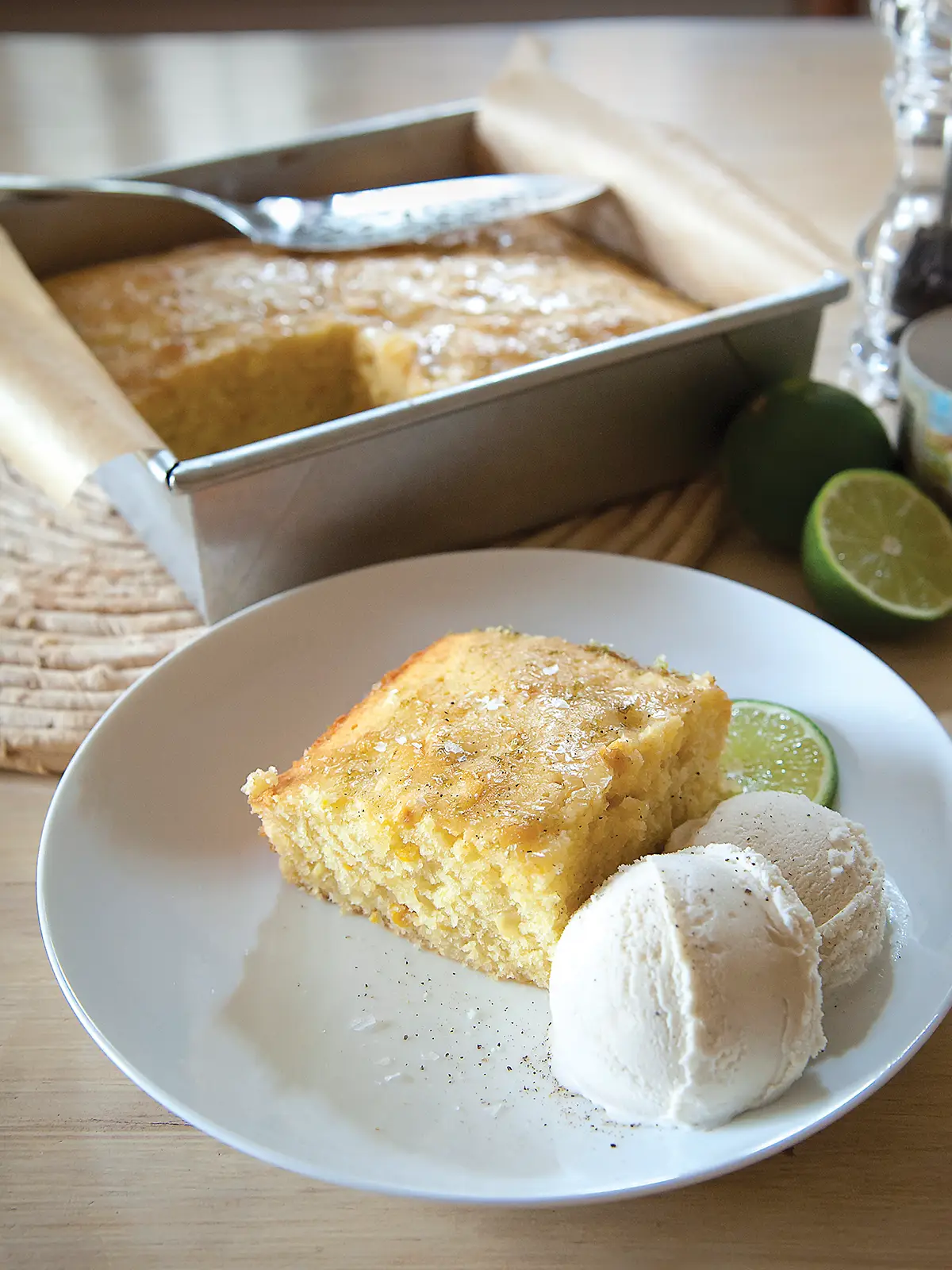 9x9 pan containing sweet corn cake with a slice removed and plated with two scoops of vanilla ice cream.