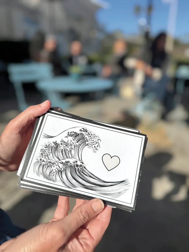 Sondra Weiss holding a postcard of a wave about to break over a heart.