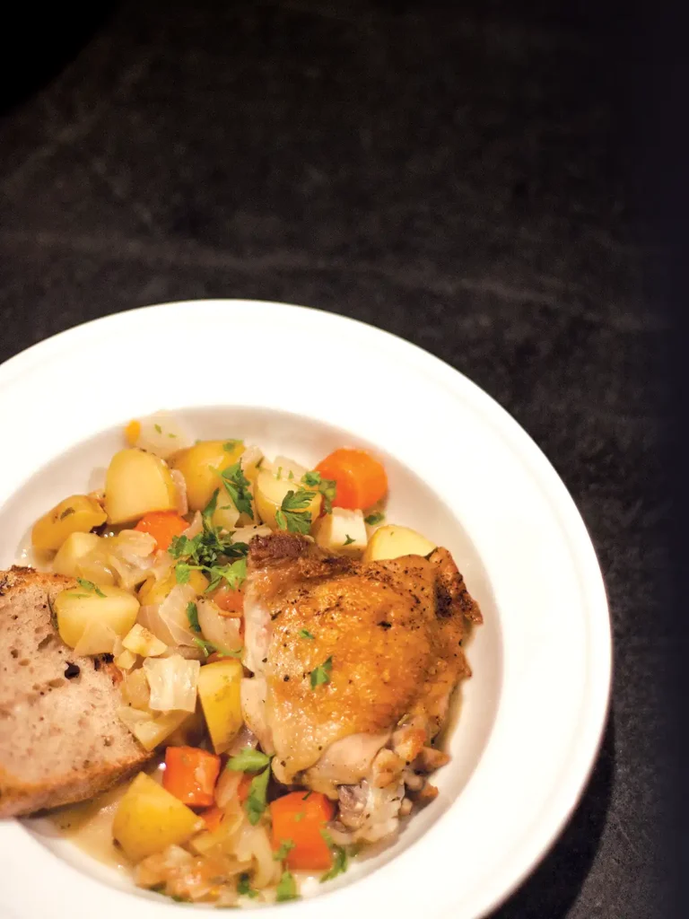 A white bowl with chicken in Sauvignon Blanc, vegetables, and bread.