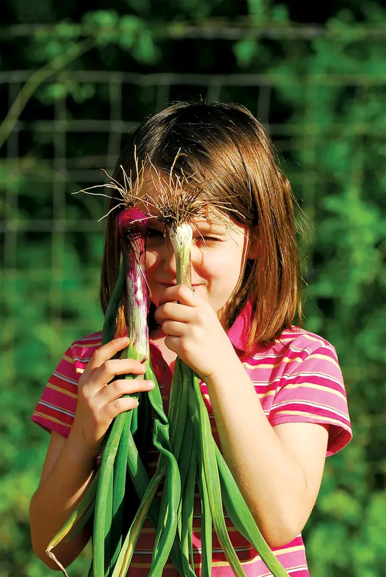 Young girl holding leeks up to her eyes.