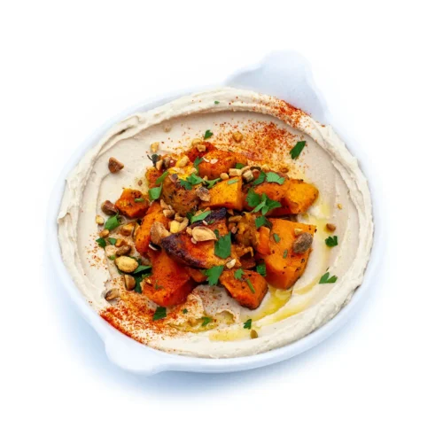 White dish with hummus tahina topped with butternut squash.