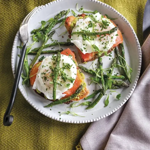 Overhead shot of a plate with two toasts with poached eggs, smoked salmon, fava bean pate, and asparagus.
