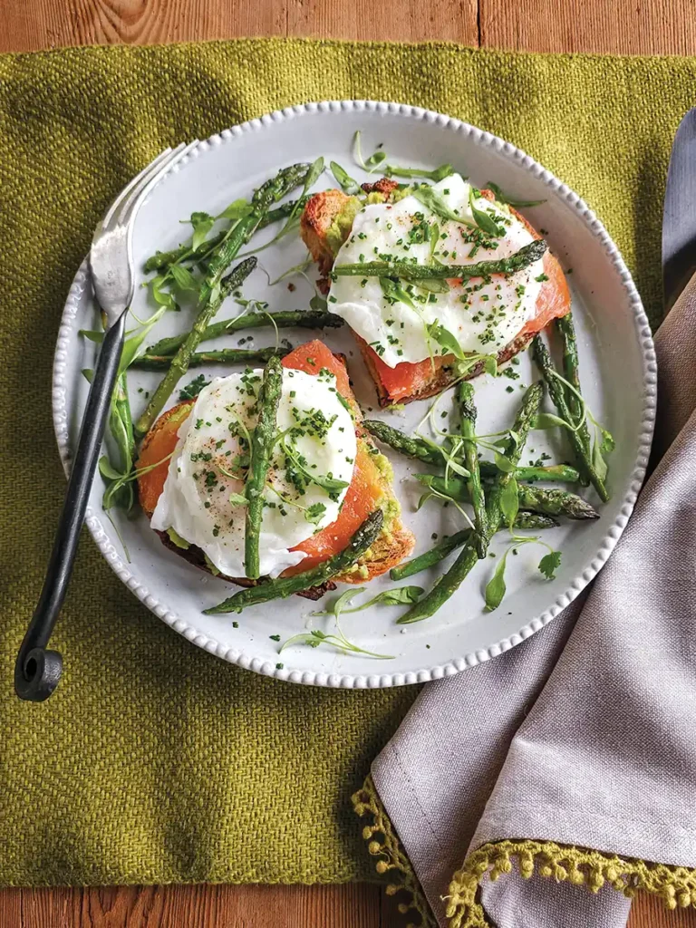 Overhead shot of a plate with two toasts with poached eggs, smoked salmon, fava bean pate, and asparagus.