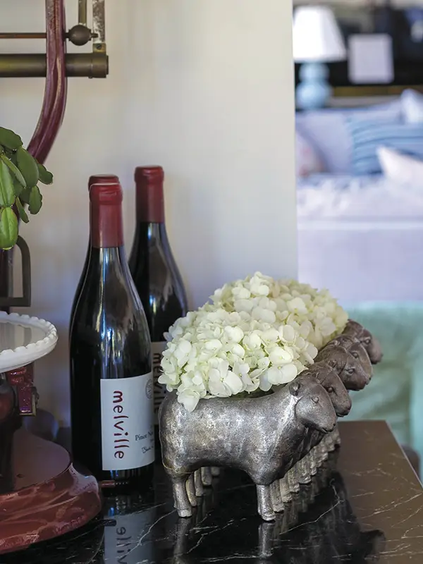 Two bottles of wine and some flowers on an end table with the bedroom in the background.