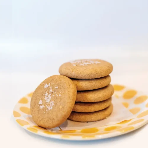 Stack of brown butter cookies on a yellow polka dotted plate against a pale blue background.