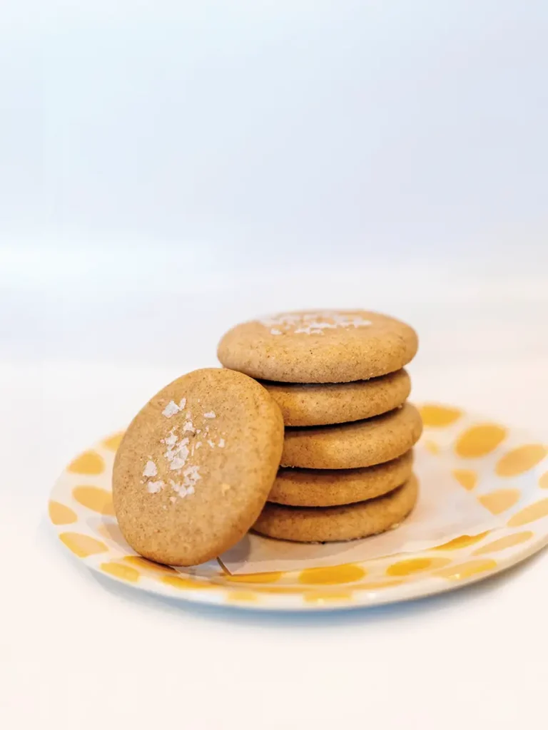 Stack of brown butter cookies on a yellow polka dotted plate against a pale blue background.