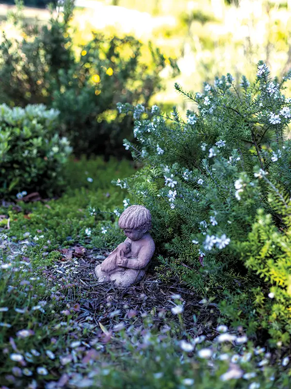 Statue of a small child holding a rabbit nestled into the garden.