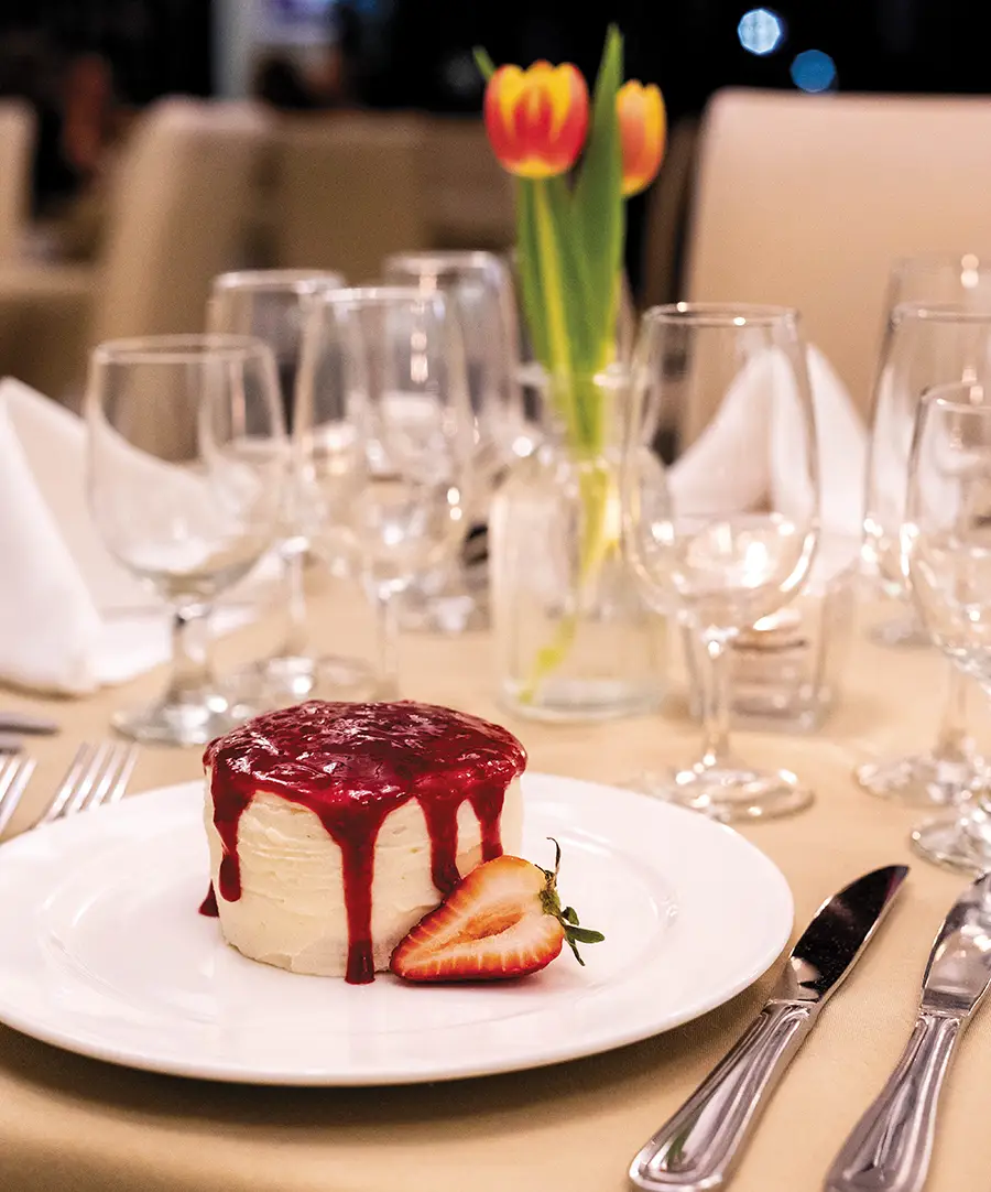 Petit mixed berry layer cake and berry coulis plated at the table.