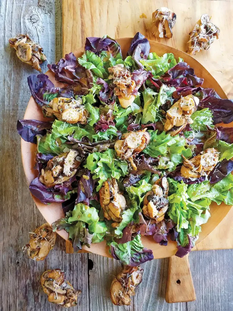 Colorful wild mushroom crostini salad set on a wooden cutting board on a wooden tabletop.