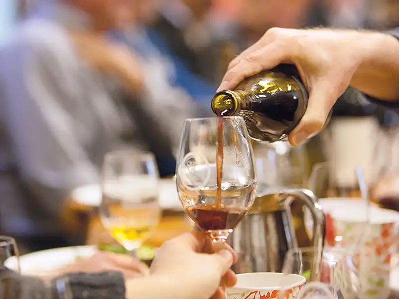 Hand pouring a glass of wine at a table.