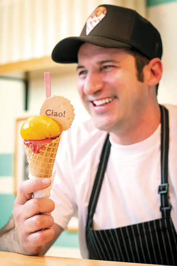 Alessio at his Solvang shop holding a gelato cone with a cookie that reads "Ciao!".