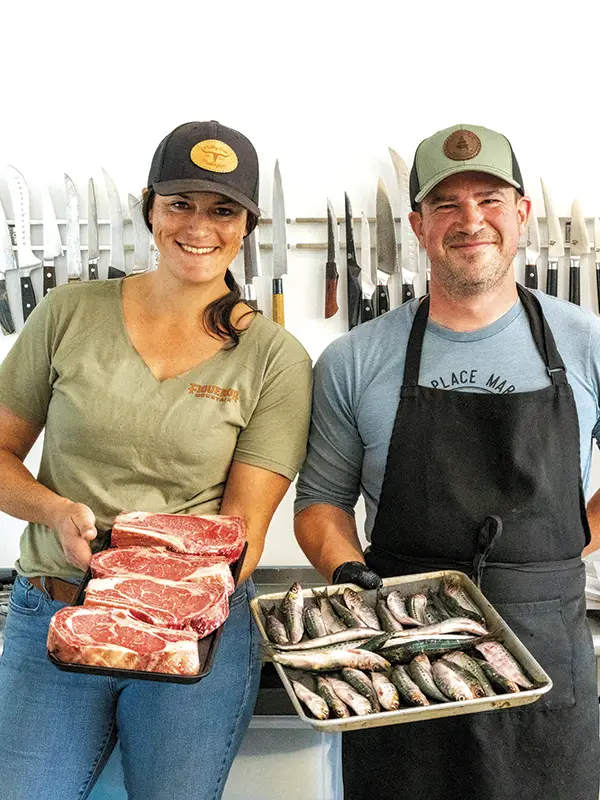 Cassidy and Marko Alexandrous hold out trays of meat and seafood at their Motley Crew Marketplace.