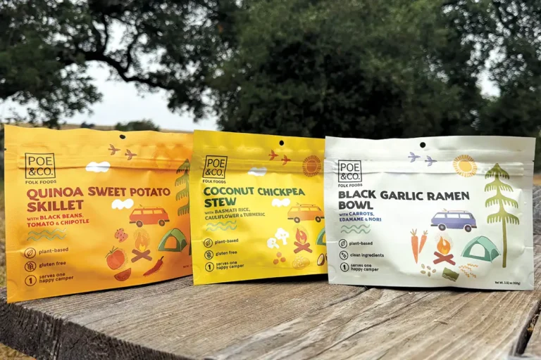 Three pouches of Poe and Co. camping meals lined up on a picnic table.