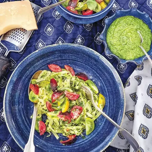 Bowl of fresh pasta with heirloom tomatoes and summer pesto in a blue bowl on a blue and white tablescape.