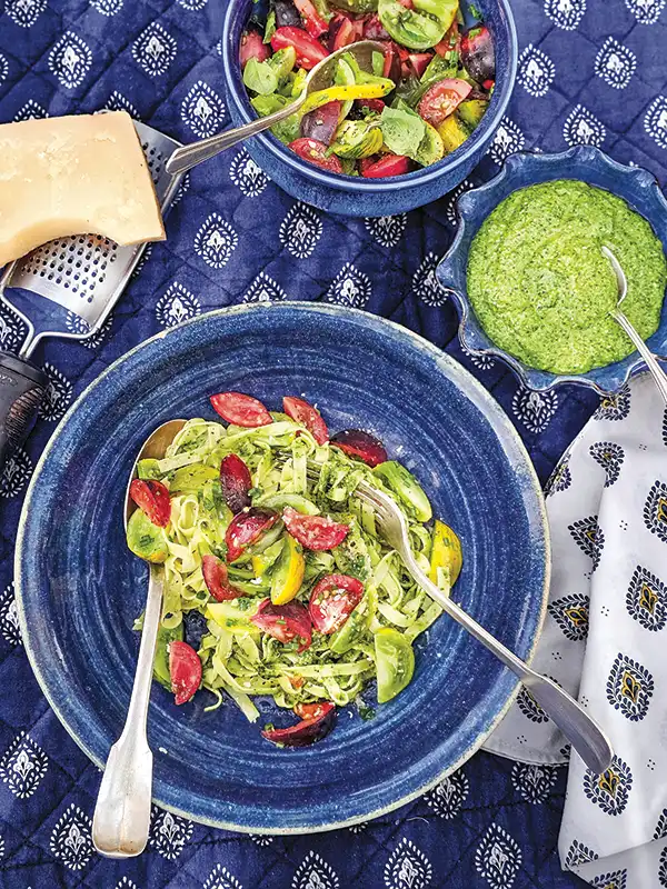 Bowl of fresh pasta with heirloom tomatoes and summer pesto in a blue bowl on a blue and white tablescape.